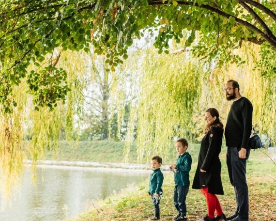 A family enjoys a peaceful walk by a lakeside under a willow tree during autumn.