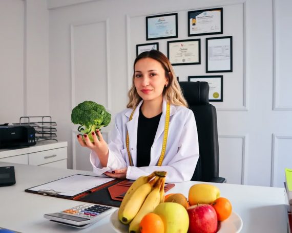 Female nutritionist in office holding broccoli, surrounded by fruits, promoting healthy lifestyle.
